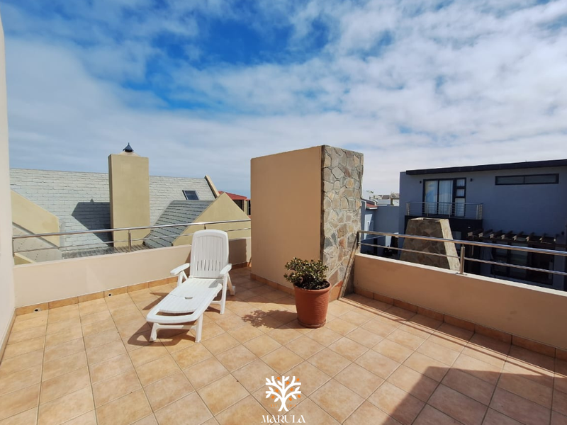 An open-air rooftop balcony featuring tiled flooring, a stone-clad feature wall, and stainless steel railings with views of the surrounding neighborhood.