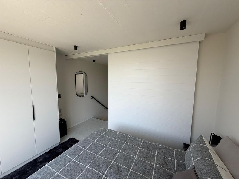 A modern bedroom featuring a large built-in wardrobe, a sliding partition door, and minimalist recessed ceiling lighting, leading to an adjacent staircase.