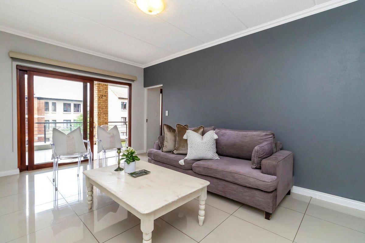 A bright living room featuring large sliding glass doors leading to a balcony, tiled flooring, and a modern dark grey accent wall.