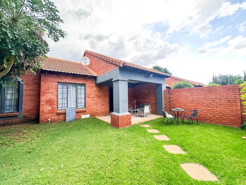 Rear view of the townhouse featuring a covered patio, private garden with a stone pathway, and a brick boundary wall.
