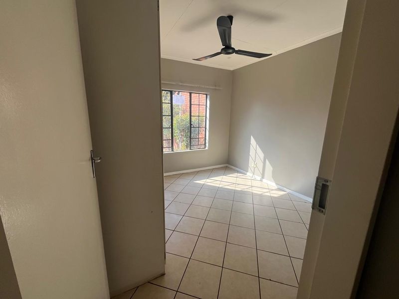 A bright, empty bedroom featuring neutral wall paint, tiled flooring, and a ceiling fan, offering a clean canvas for personalization.