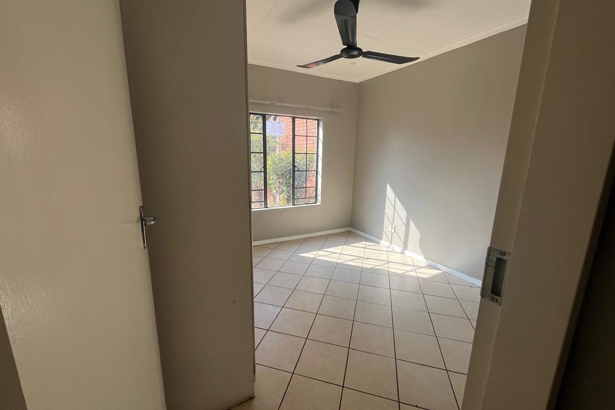 A bright, empty bedroom featuring neutral wall paint, tiled flooring, and a ceiling fan, offering a clean canvas for personalization.
