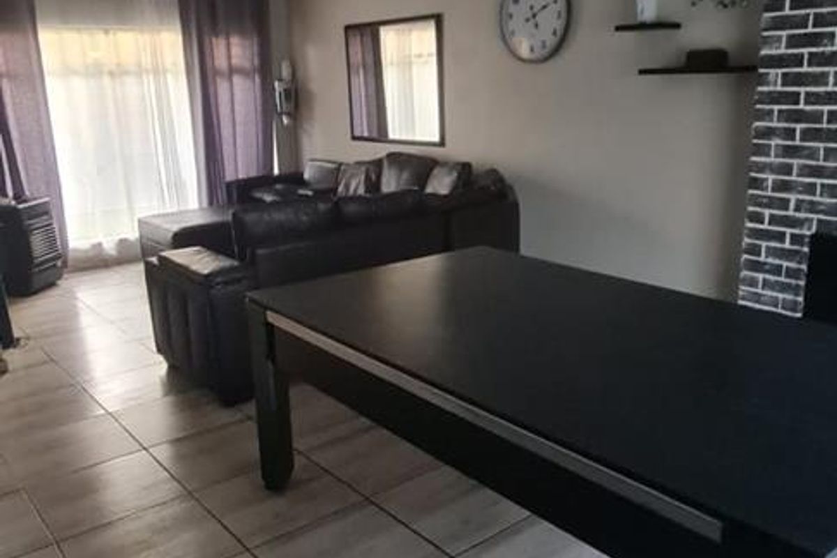 Spacious living area featuring modern tiled flooring, a striking brick feature wall, and contemporary pendant lighting with access to the outdoors.