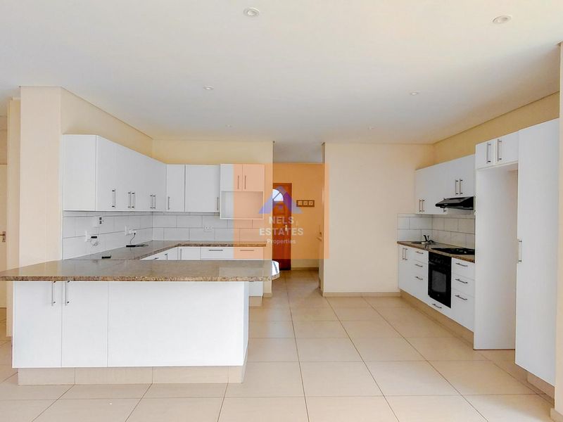 Spacious open-plan kitchen featuring white built-in cabinetry, granite countertops, integrated oven and hob, and tiled flooring throughout.