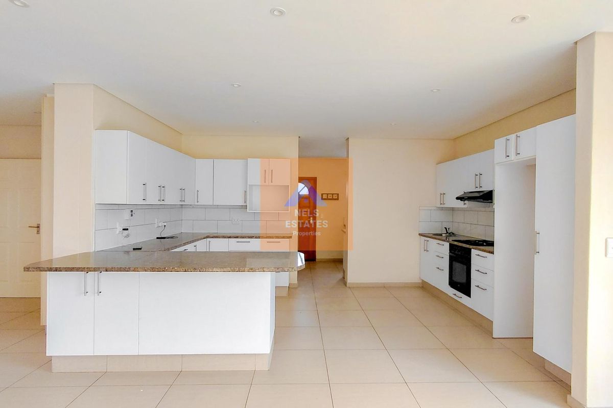 Spacious open-plan kitchen featuring white built-in cabinetry, granite countertops, integrated oven and hob, and tiled flooring throughout.