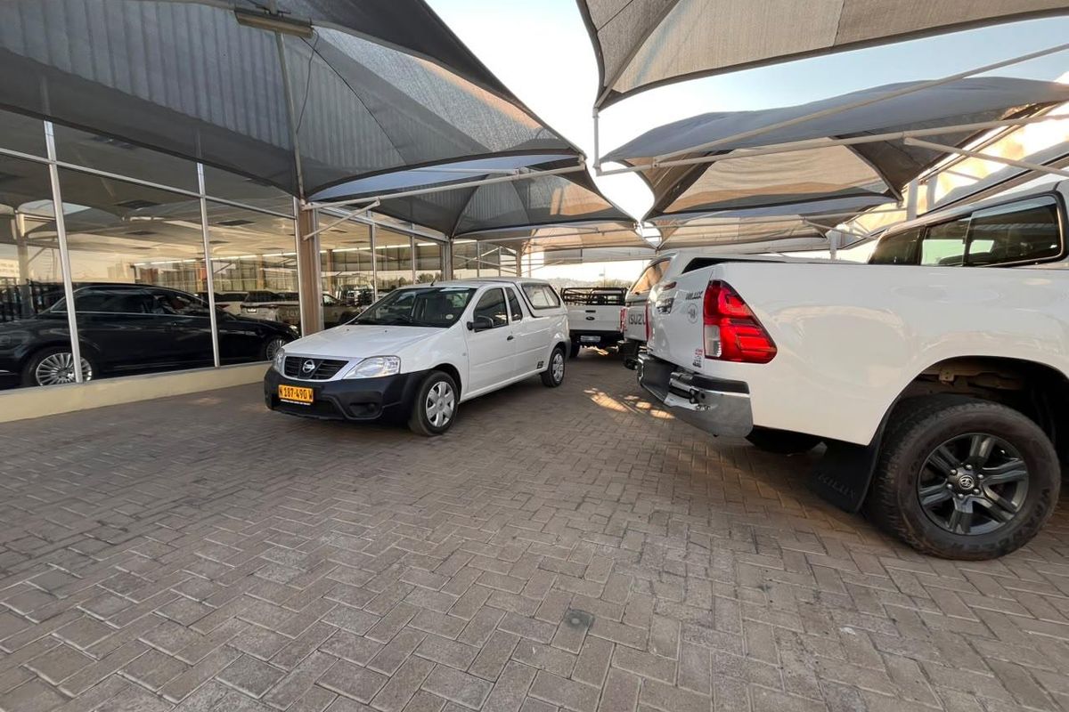 A commercial retail exterior featuring a paved parking area covered by shade cloth canopies and a large glass storefront facade.