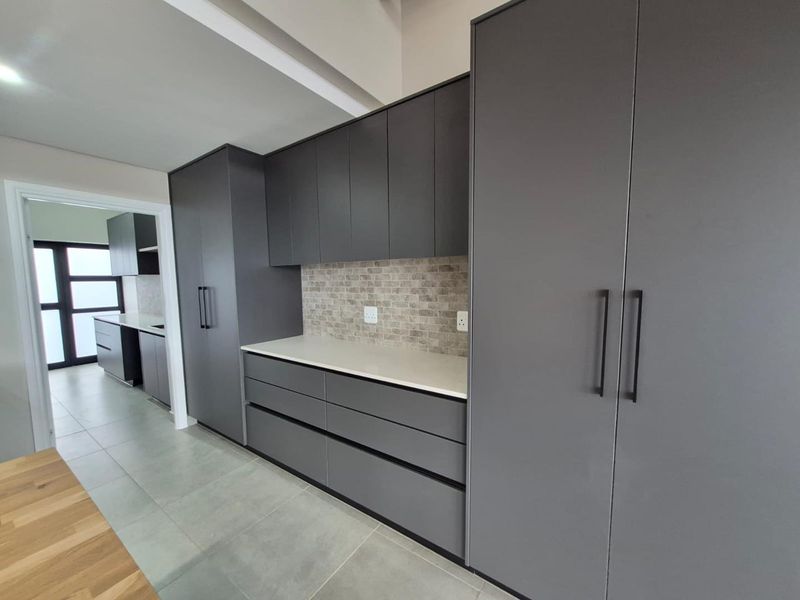 Modern kitchen featuring sleek dark grey cabinetry, stone countertops, and a textured tiled backsplash with neutral floor tiles.