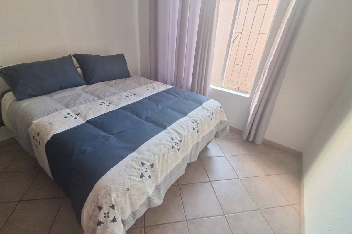 A functional bedroom featuring tiled flooring and a window fitted with security bars, providing natural light and basic security.