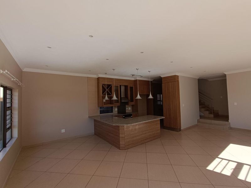 Spacious open-plan living area featuring a modern kitchen with granite countertops, built-in cabinetry, and a central island, leading to an adjacent staircase.