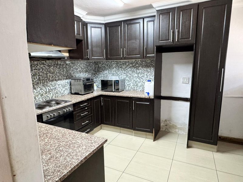 Kitchen featuring dark wood cabinetry, granite countertops, and a mosaic tile backsplash, with a dedicated fridge cavity and built-in oven and hob.