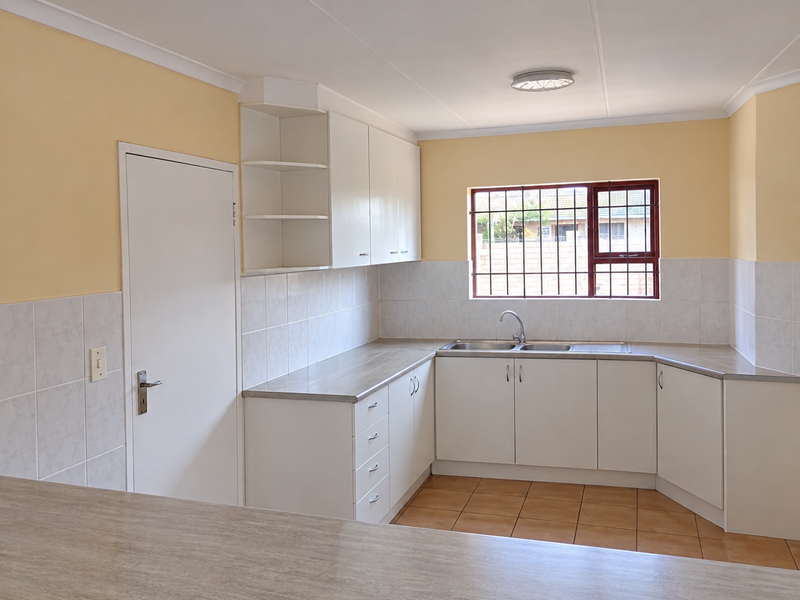 A clean, empty kitchen featuring white built-in cabinetry, laminate countertops, a double sink, and tiled backsplash with neutral wall finishes.