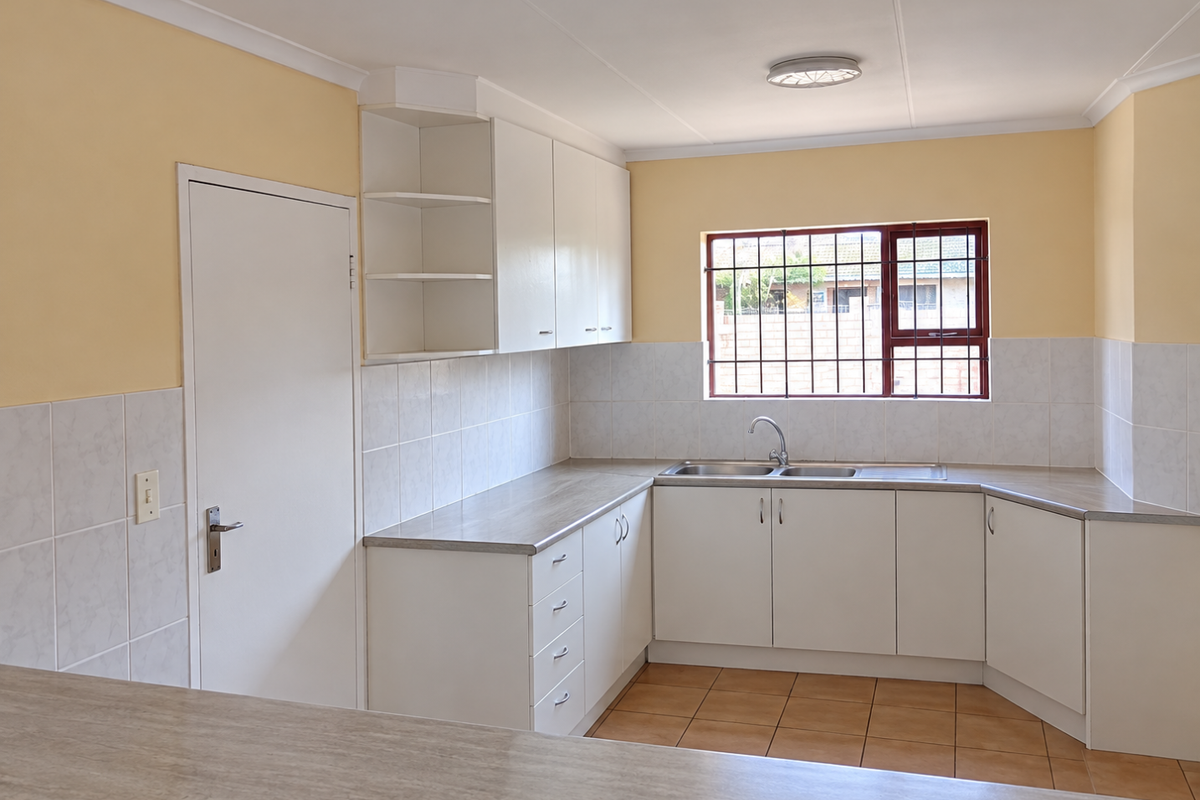 A clean, empty kitchen featuring white built-in cabinetry, laminate countertops, a double sink, and tiled backsplash with neutral wall finishes.