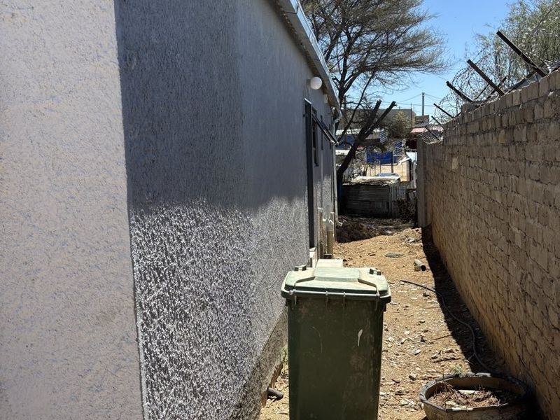 A narrow side passage of the property featuring a textured exterior wall, guttering, and a perimeter brick wall topped with security razor wire.