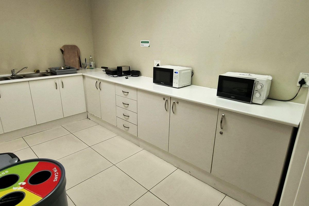 A functional office kitchenette featuring white cabinetry, a stainless steel sink, and tiled flooring, providing a clean and practical space for staff use.