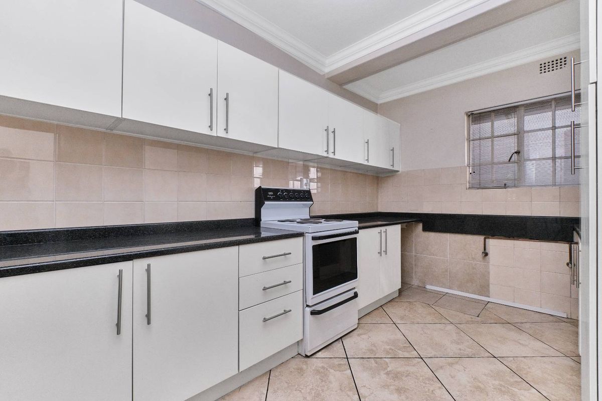 A functional kitchen featuring white cabinetry, black granite countertops, tiled backsplash, and a freestanding stove, with neutral ceramic floor tiles throughout.