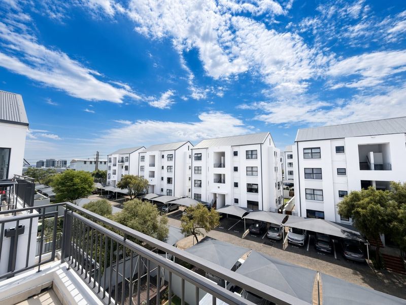 Elevated view overlooking a modern apartment complex with white facades, pitched roofs, and designated covered parking areas.
