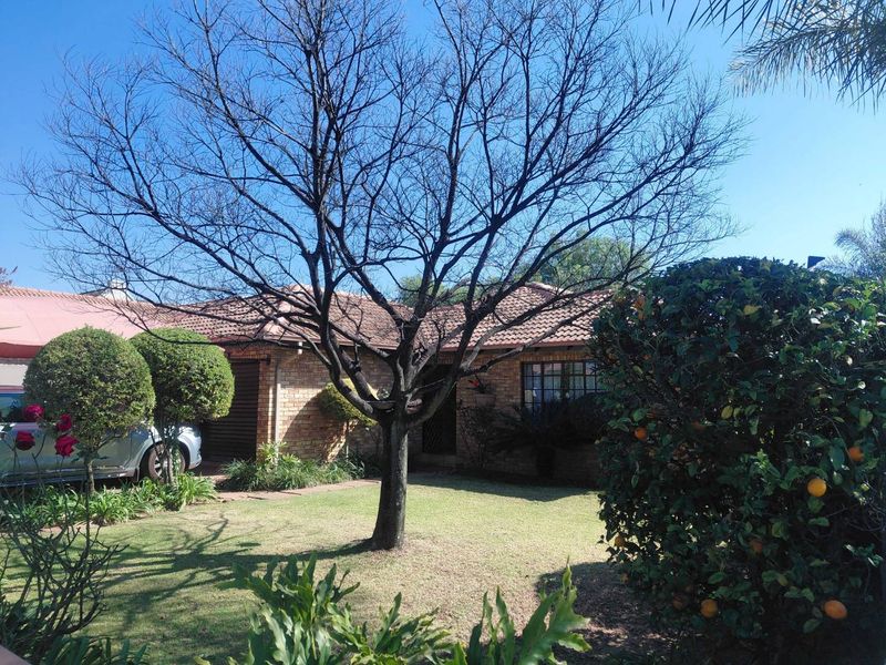 Front view of a brick house featuring a tiled roof, attached garage, and a well-maintained front garden with mature trees.