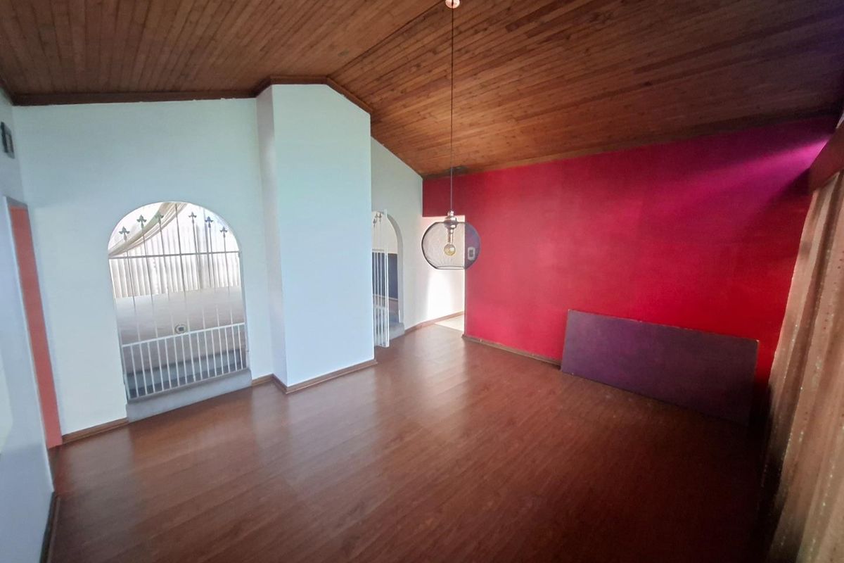 An empty living room featuring a vaulted timber ceiling, laminate flooring, and distinctive arched doorways with security gates.