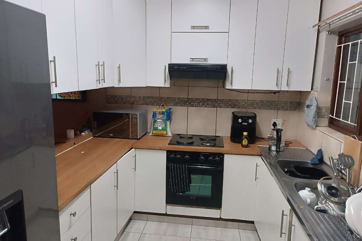 Compact kitchen featuring white cabinetry, wood-look laminate countertops, built-in oven with hob, extractor fan, and a double-basin stainless steel sink.
