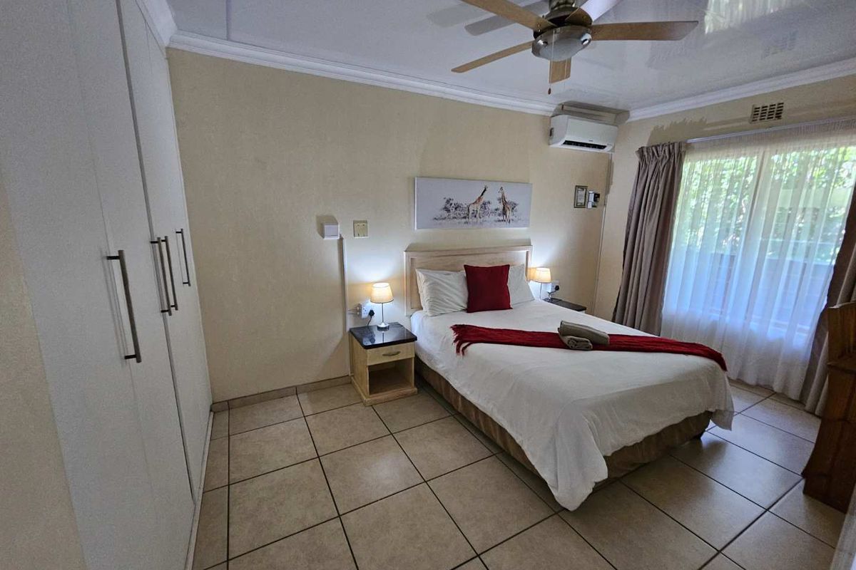 A bedroom featuring tiled flooring, built-in cupboards, a ceiling fan, and a wall-mounted air conditioning unit.