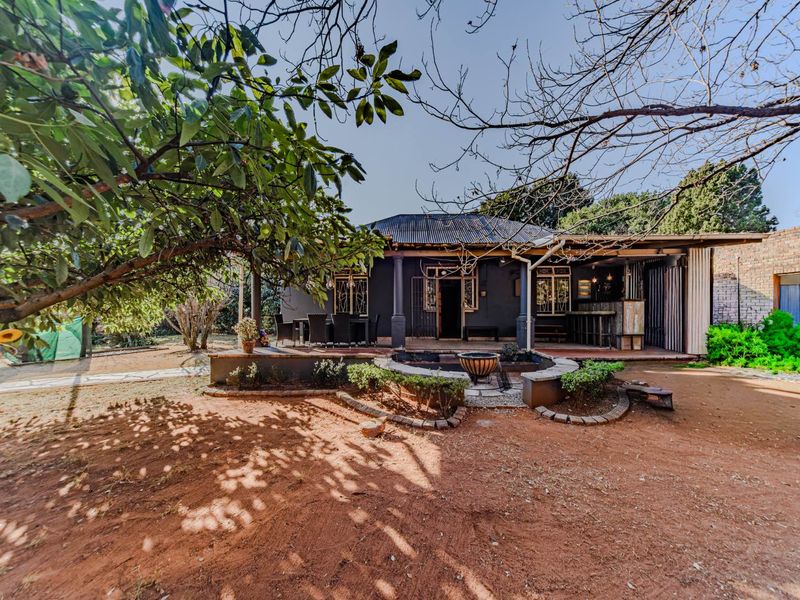 Rear view of the house featuring a covered patio area with a built-in bar, overlooking a garden with mature trees and a brick retaining wall.