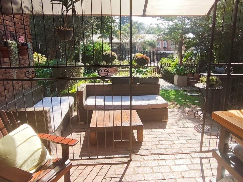 A covered patio area featuring brick paving, an exposed brick wall, and a security gate, overlooking a private garden space.