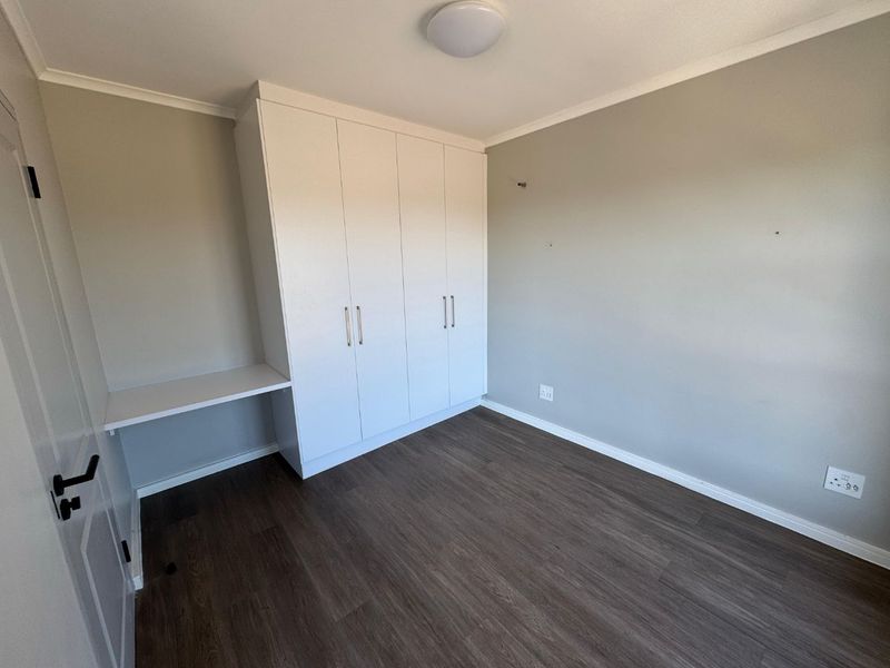 A clean, empty bedroom featuring modern laminate flooring, built-in white cupboards, and an integrated desk area, ready for personalization.