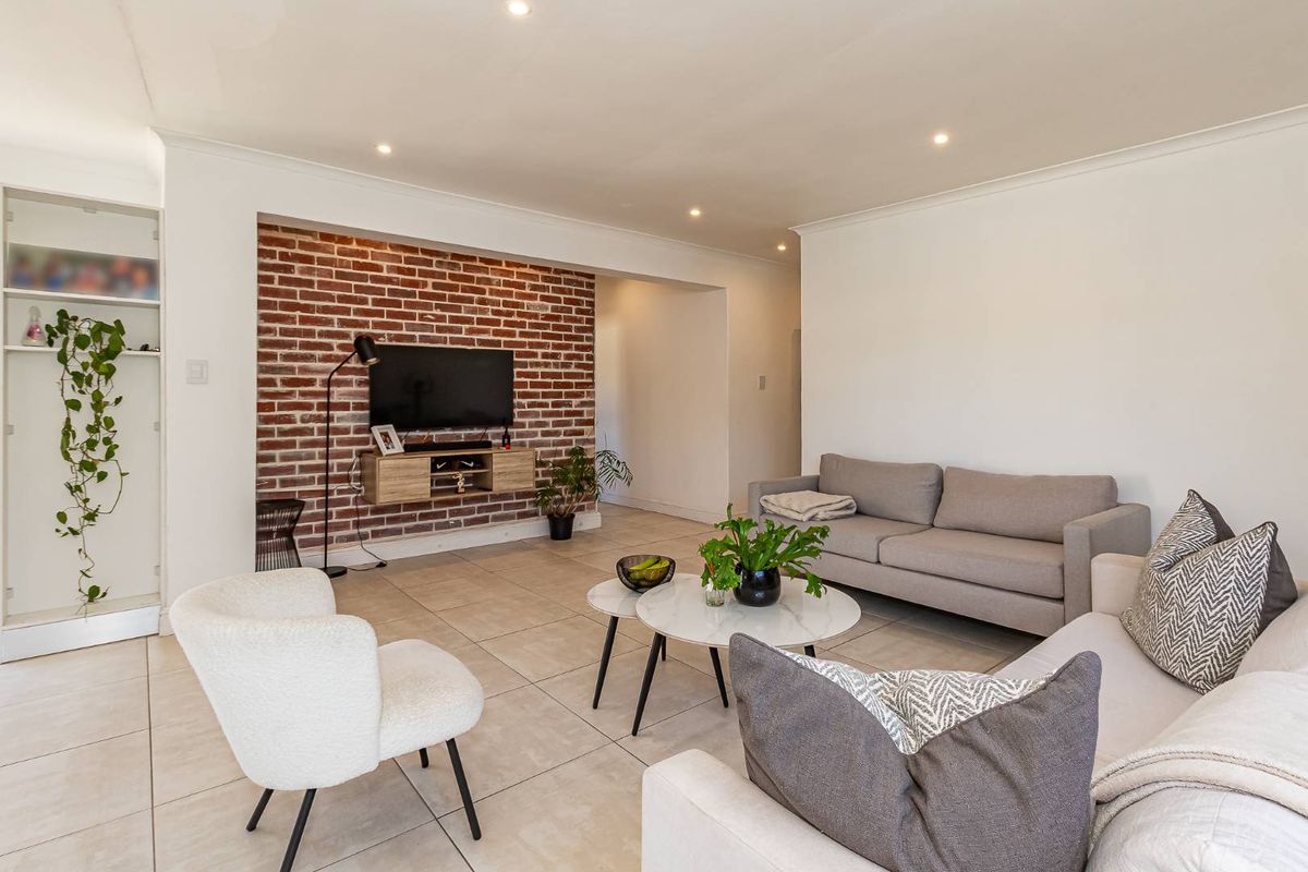 Spacious living room featuring a prominent exposed brick feature wall, neutral floor tiles, and recessed downlighting.