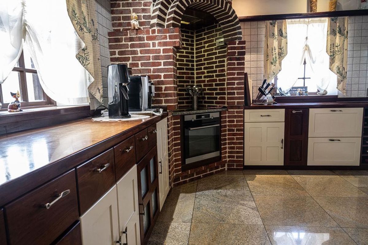 A rustic-style kitchen featuring a brick-encased built-in oven, polished stone flooring, and a combination of dark wood and white cabinetry.