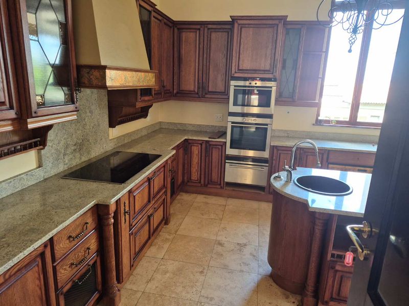 A traditional kitchen featuring dark wood cabinetry, granite countertops, a built-in double oven, and a central island with an undermount sink.