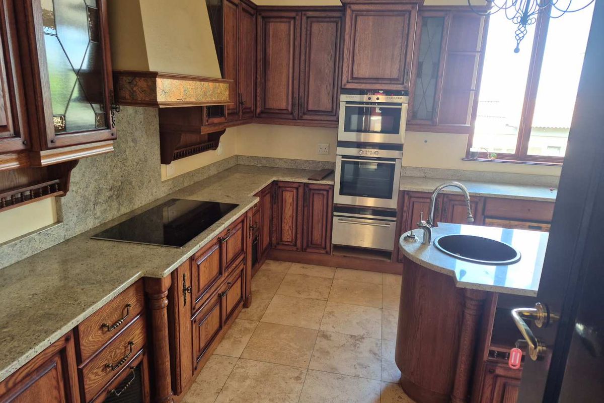 A traditional kitchen featuring dark wood cabinetry, granite countertops, a built-in double oven, and a central island with an undermount sink.