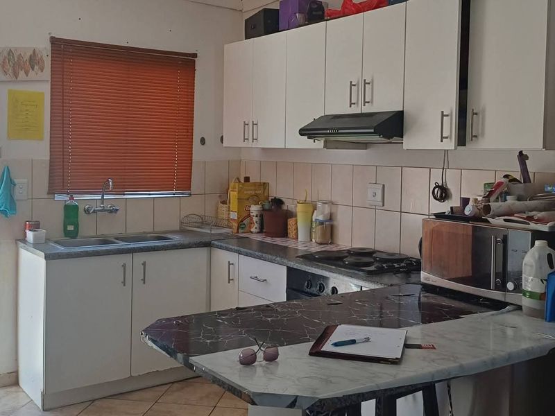 Functional kitchen featuring white cabinetry, tiled backsplash, built-in hob and oven, and a double sink with direct access to an outdoor area.