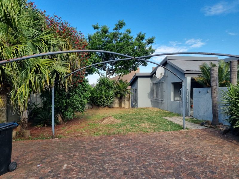 Front exterior view of the property featuring a paved driveway, a metal carport frame, and a lawn area with established garden landscaping.