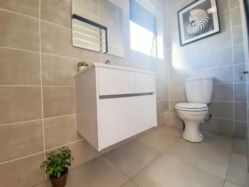 Modern bathroom featuring a wall-mounted vanity, neutral floor-to-ceiling wall tiles, and a standard ceramic toilet.