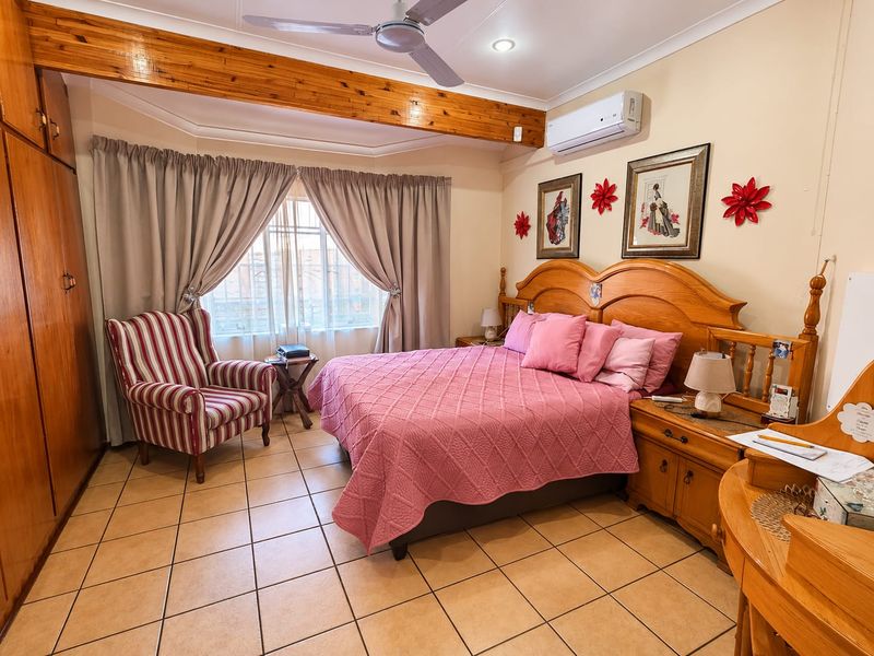 A spacious bedroom featuring tiled flooring, a built-in wooden wardrobe, an exposed timber ceiling beam, and a wall-mounted air conditioning unit.