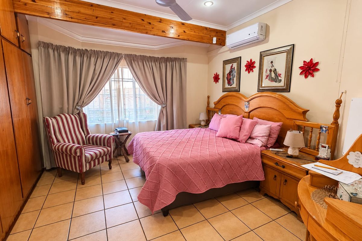 A spacious bedroom featuring tiled flooring, a built-in wooden wardrobe, an exposed timber ceiling beam, and a wall-mounted air conditioning unit.