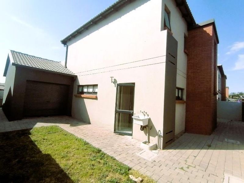 Rear view of the townhouse featuring a paved courtyard, attached garage, and an external utility sink area.