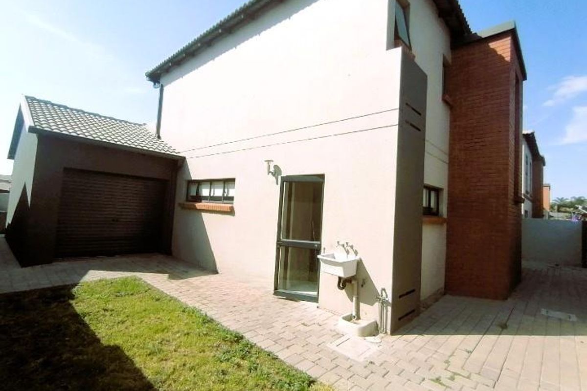 Rear view of the townhouse featuring a paved courtyard, attached garage, and an external utility sink area.