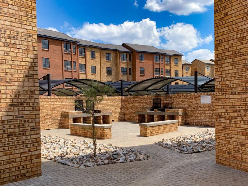 Communal outdoor entertainment area featuring built-in brick braai stands, paved flooring, and covered seating structures within a secure apartment complex.