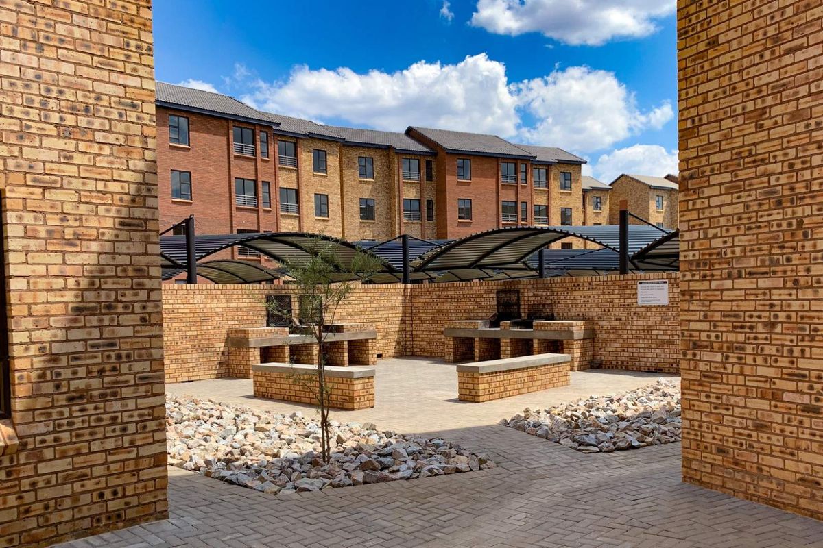 Communal outdoor entertainment area featuring built-in brick braai stands, paved flooring, and covered seating structures within a secure apartment complex.