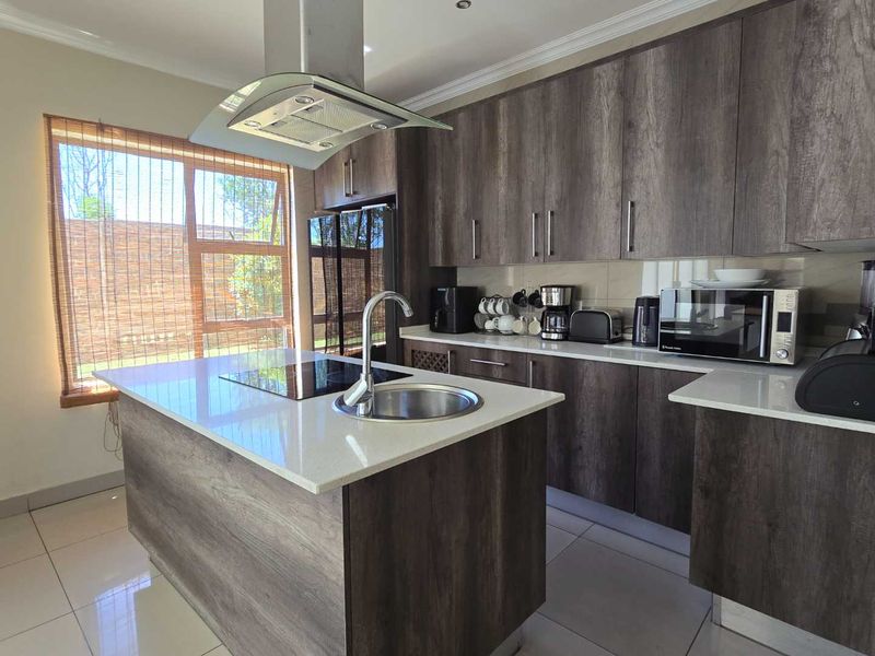 Modern kitchen featuring dark wood-grain cabinetry, white quartz countertops, a central island with a built-in hob, and high-quality stainless steel fixtures.