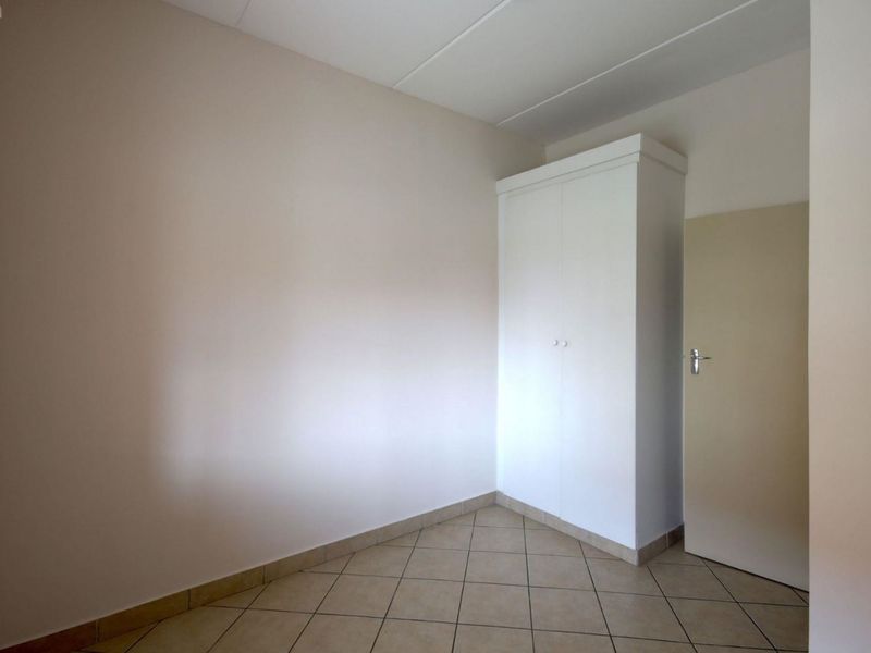 An empty bedroom featuring neutral walls, tiled flooring, and a built-in white wardrobe.