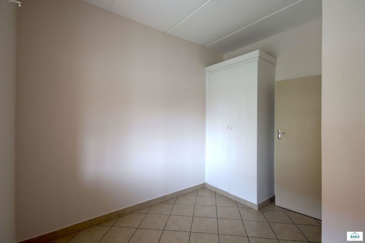 An empty bedroom featuring neutral walls, tiled flooring, and a built-in white wardrobe.