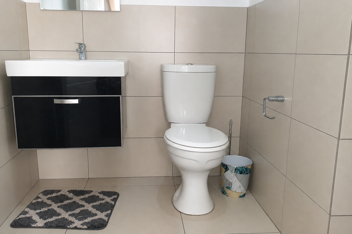 A clean, modern bathroom featuring a wall-mounted vanity with a basin and a standard toilet, finished with neutral floor-to-ceiling wall tiles.