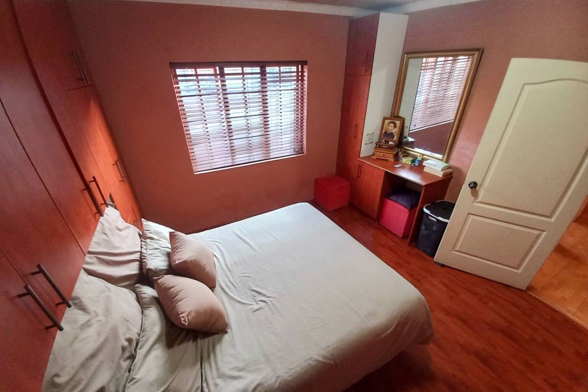 A bedroom featuring built-in wooden cabinetry, laminate flooring, and a window with fitted blinds.
