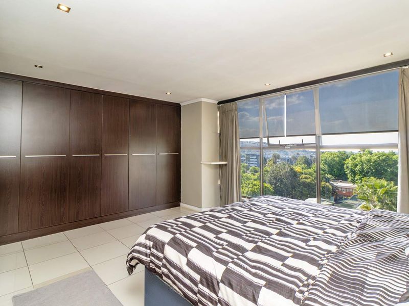 Spacious bedroom featuring extensive built-in dark wood cabinetry, large windows offering scenic views, and modern tiled flooring with recessed lighting.