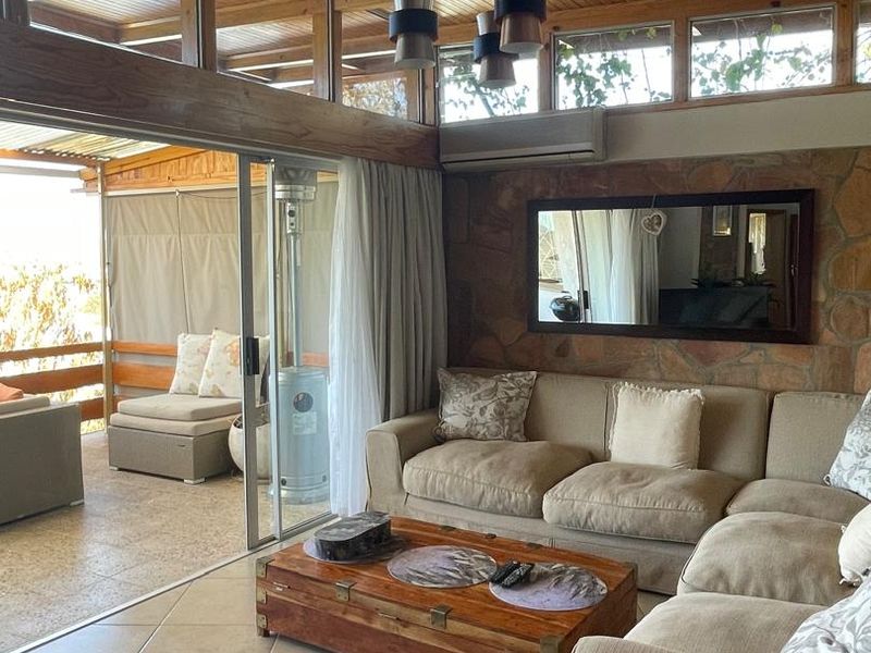 Spacious living room featuring a vaulted timber ceiling, stone feature wall, and large sliding doors opening onto an adjacent patio area.