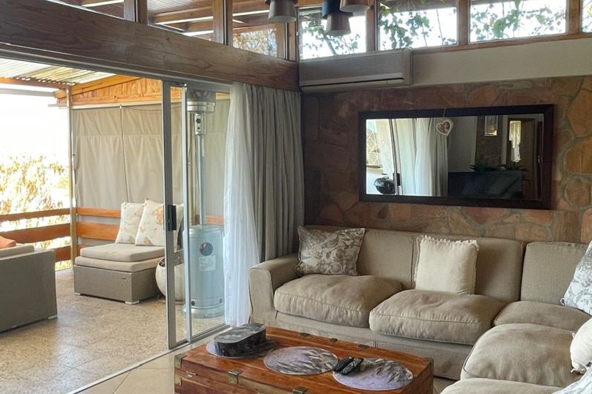Spacious living room featuring a vaulted timber ceiling, stone feature wall, and large sliding doors opening onto an adjacent patio area.