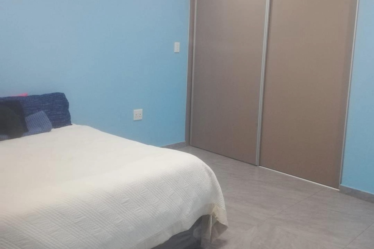 A bedroom featuring light blue walls, large format floor tiles, and built-in sliding door cupboards.