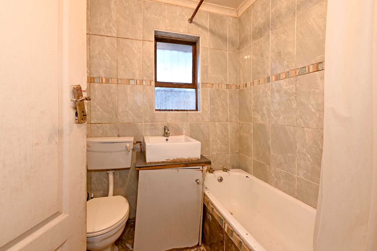 A compact bathroom featuring a bathtub, toilet, and washbasin with tiled walls, requiring cosmetic updates and maintenance to improve its overall condition.